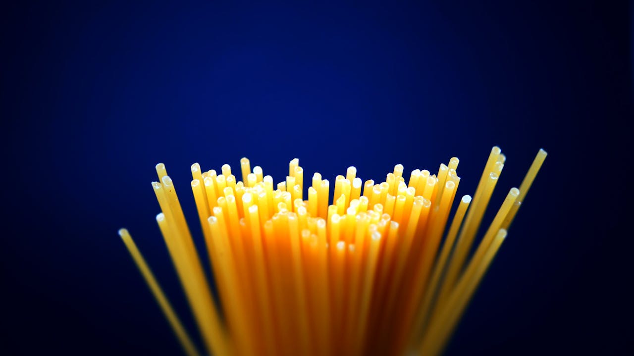 Close-up of uncooked spaghetti on a dark blue background, showcasing texture.